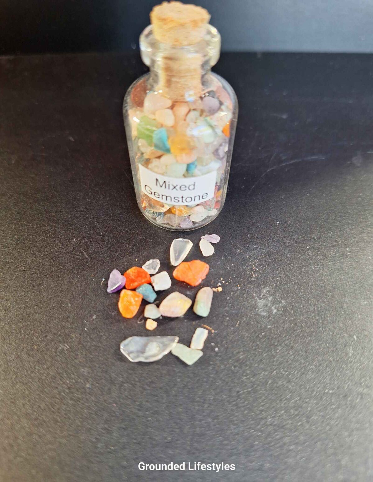 Clear bottle filled with assorted mixed gemstone grains of various colors