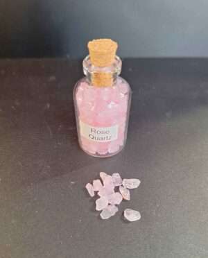 Clear bottle filled with polished rose quartz gemstone grains