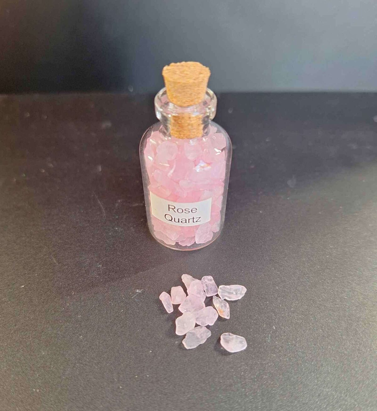 Clear bottle filled with polished rose quartz gemstone grains